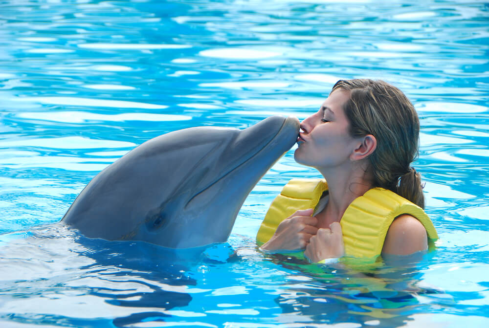 A woman giving a dolphin a kiss, one of the many encounters with animals to enjoy in the Bahamas.